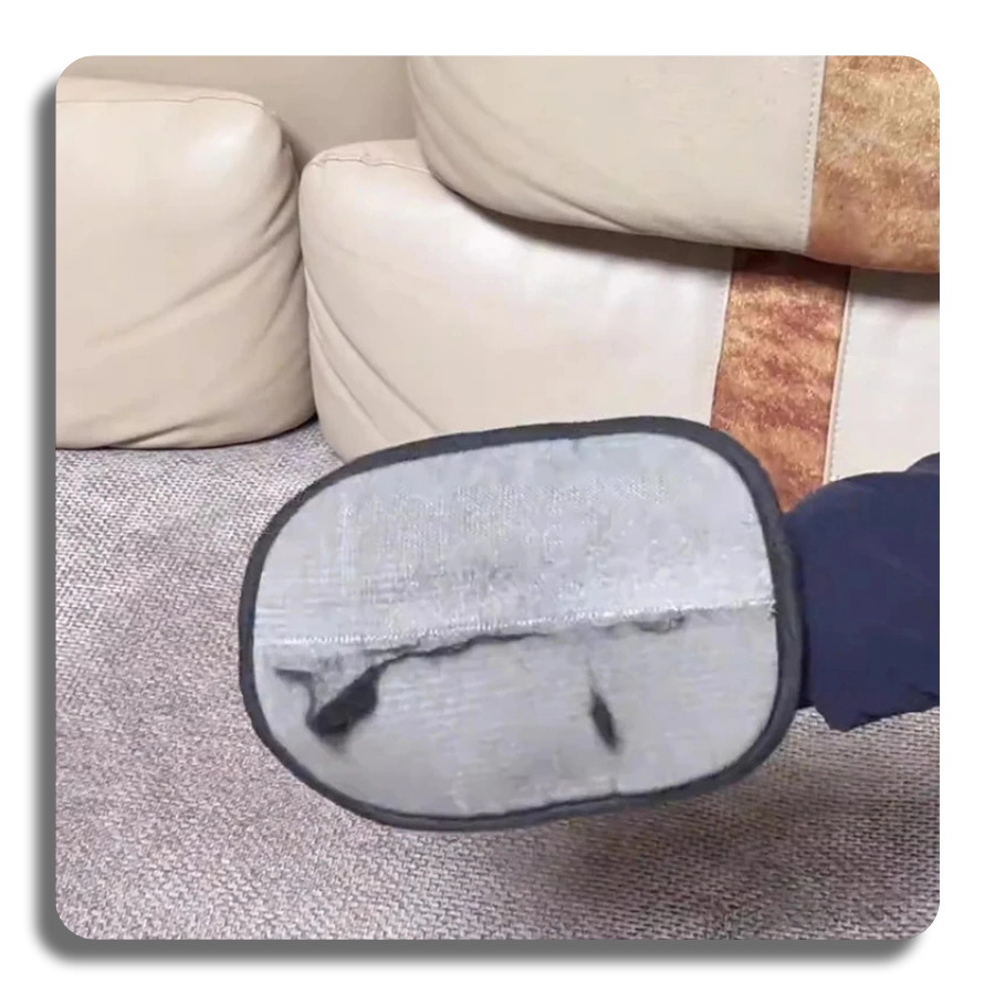 A close-up of the grey side of the grooming glove being used to swipe away pet hair from a light-colored sofa or upholstery.